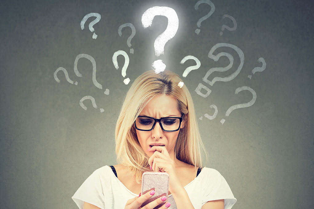 Confused woman looking at phone surrounded by question marks